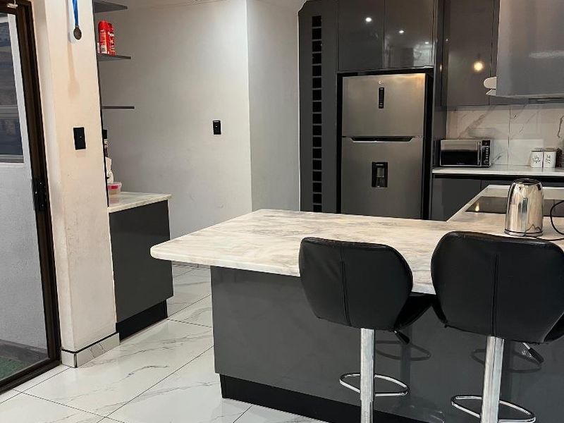 Modern kitchen featuring grey gloss cabinetry, marble-look countertops, matching floor tiles, and contemporary pendant lighting with integrated appliances.