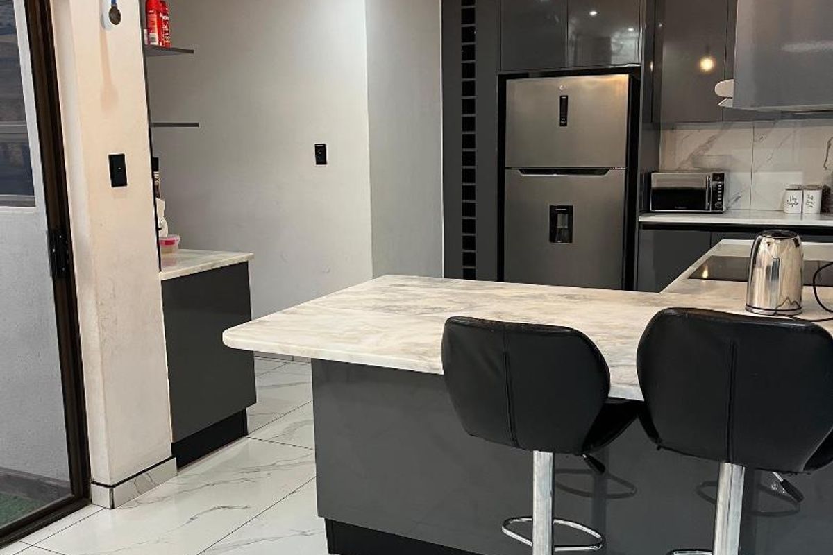 Modern kitchen featuring grey gloss cabinetry, marble-look countertops, matching floor tiles, and contemporary pendant lighting with integrated appliances.