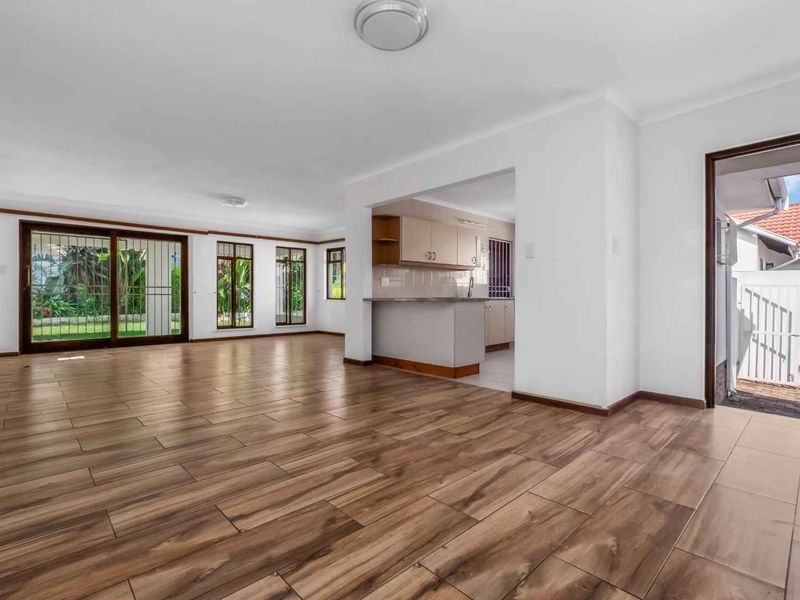 Spacious open-plan living area featuring wood-look tile flooring, neutral walls, and direct access to the garden through sliding glass doors.