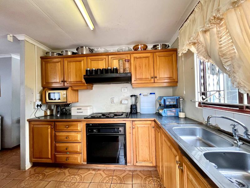 A functional kitchen featuring traditional wooden cabinetry, a built-in oven with hob, and a double stainless steel sink, offering potential for modern updates.