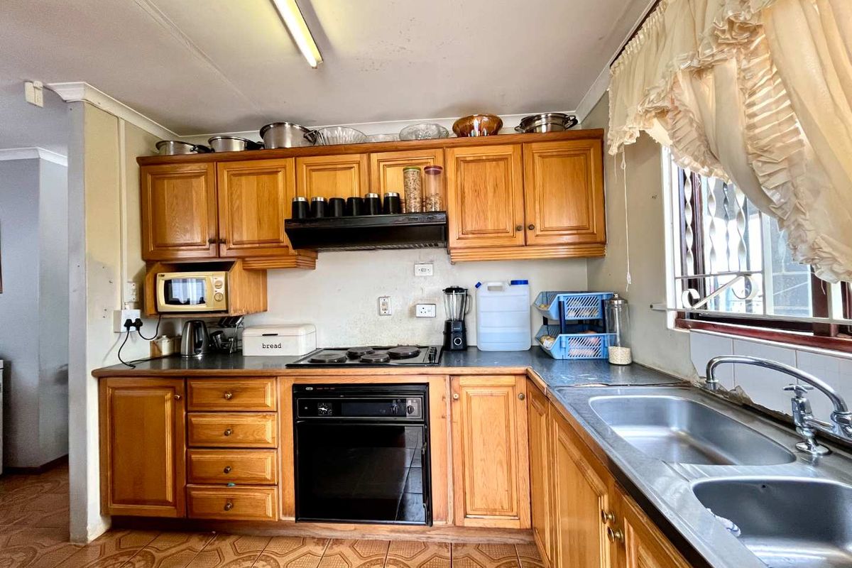 A functional kitchen featuring traditional wooden cabinetry, a built-in oven with hob, and a double stainless steel sink, offering potential for modern updates.