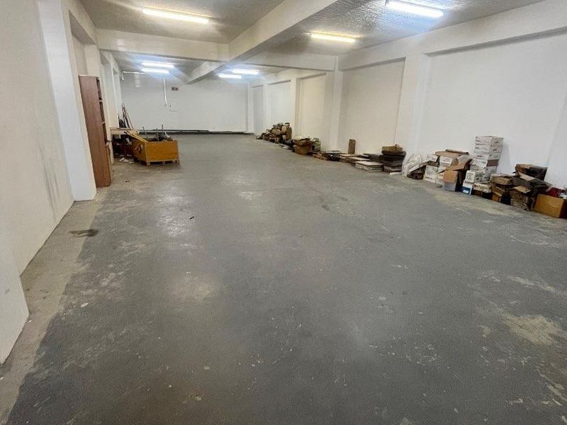 A large, open-plan utility or storage space featuring concrete flooring, exposed structural beams, and overhead fluorescent lighting, suitable for various commercial or industrial uses.