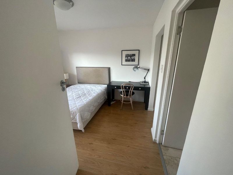 A functional bedroom featuring light wood-look laminate flooring and neutral walls, providing a clean and simple living space.