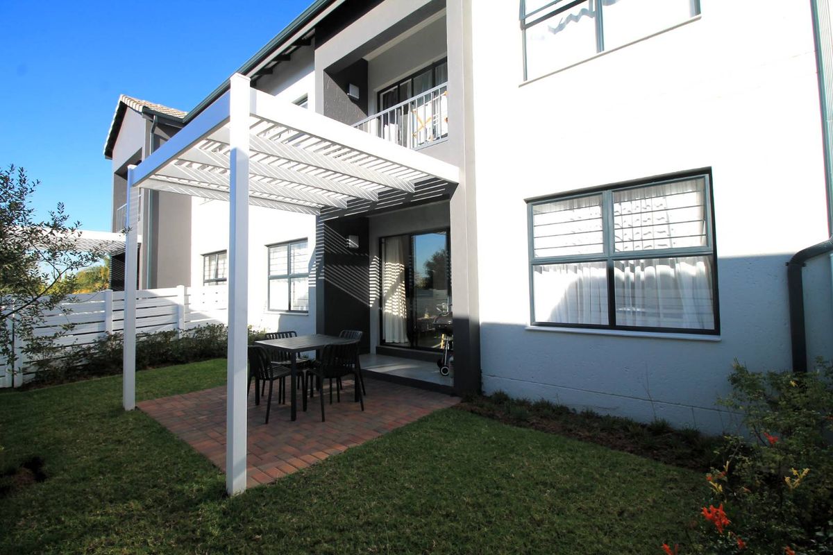 Rear view of the apartment featuring a paved patio area with a white pergola, sliding glass doors, and a small private garden.