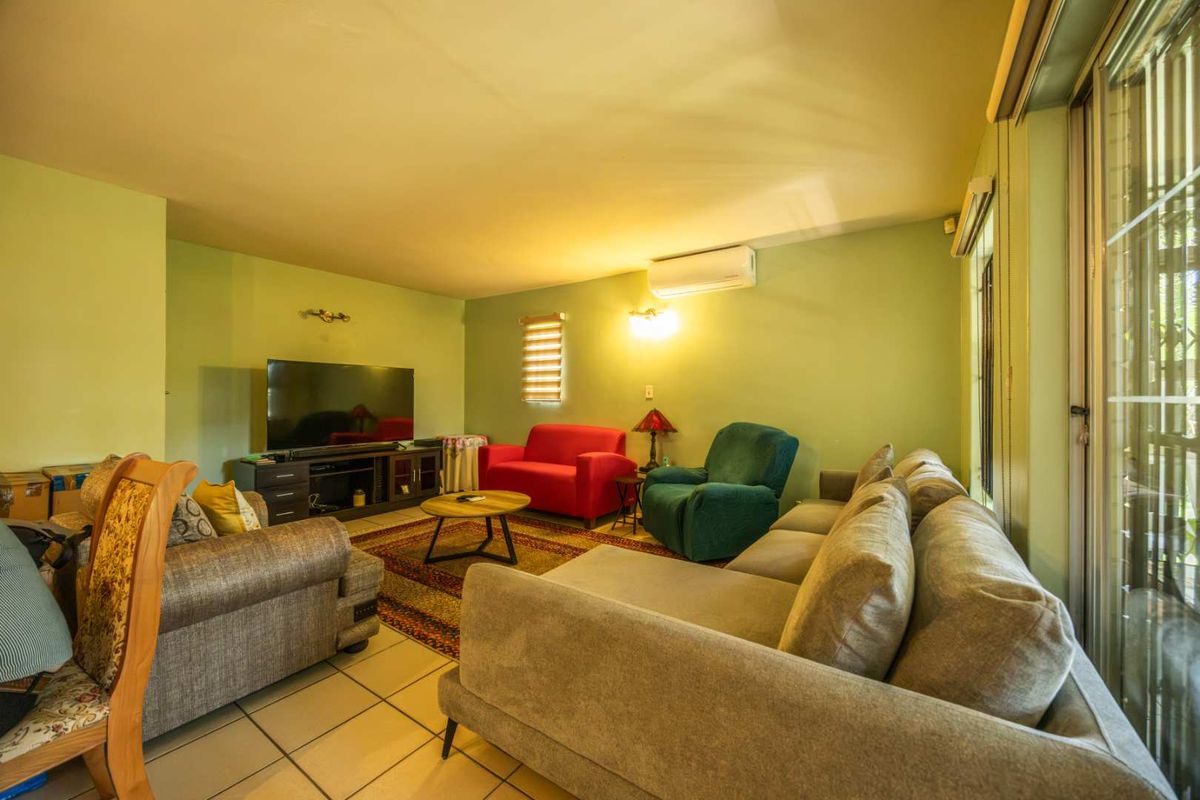 A spacious living room featuring tiled flooring, a split-system air conditioner, and large sliding glass doors that provide access to the outdoor area.