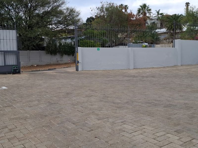A paved parking area featuring a secure perimeter wall and metal gate access, providing functional off-street parking for the office property.