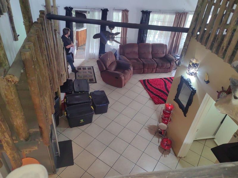 Spacious living area featuring tiled flooring, exposed timber pole staircase detailing, and a high ceiling with an exposed structural beam.