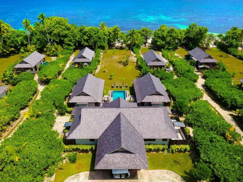 Aerial view of a luxury villa complex featuring multiple detached units, lush tropical landscaping, and a central swimming pool near the ocean.