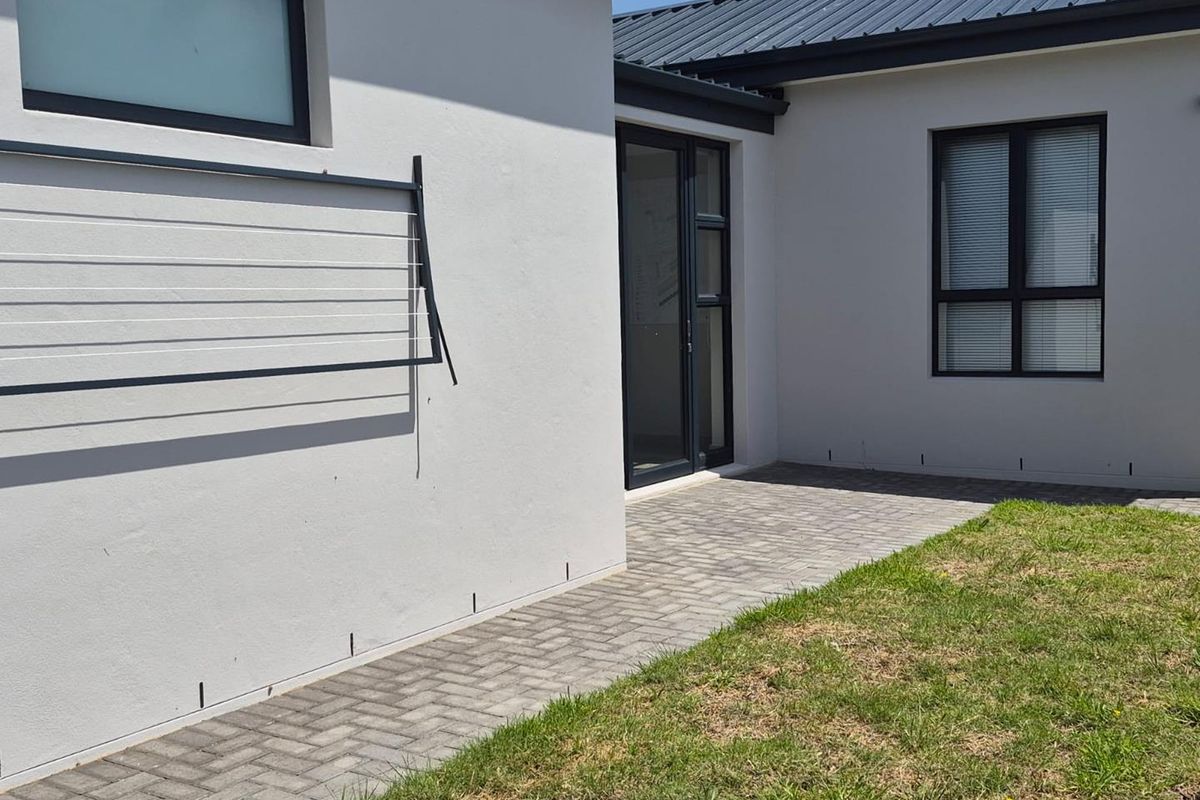 A clean rear exterior view featuring a paved walkway, manicured lawn, and modern aluminium window and door frames.