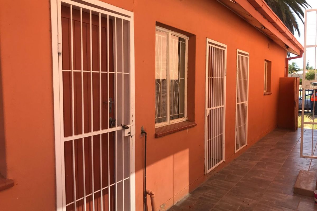 Rear exterior view of the property featuring a tiled patio area, multiple security gates, and exposed exterior wall finishes.