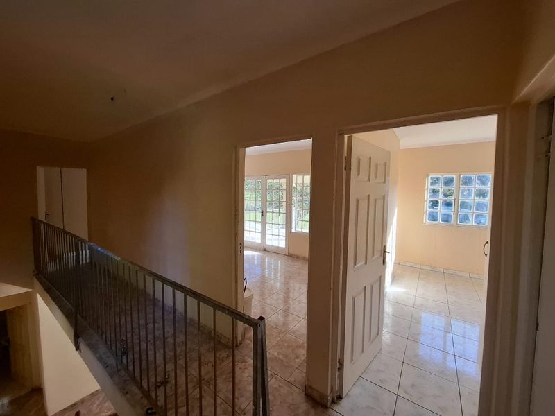 A vacant upper-level hallway featuring tiled flooring, a metal balustrade, and access to adjacent rooms with natural light.