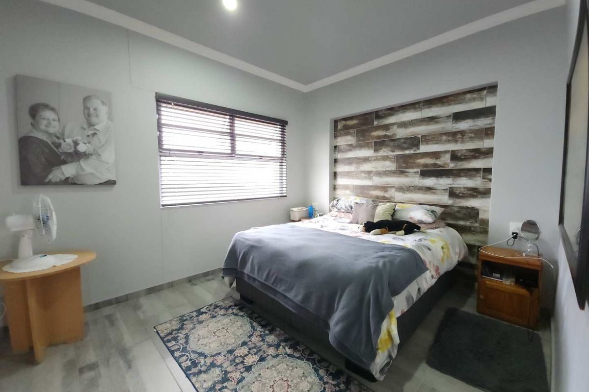 A well-maintained bedroom featuring a decorative wood-look tiled feature wall behind the bed, neutral wall tones, and modern floor tiling.