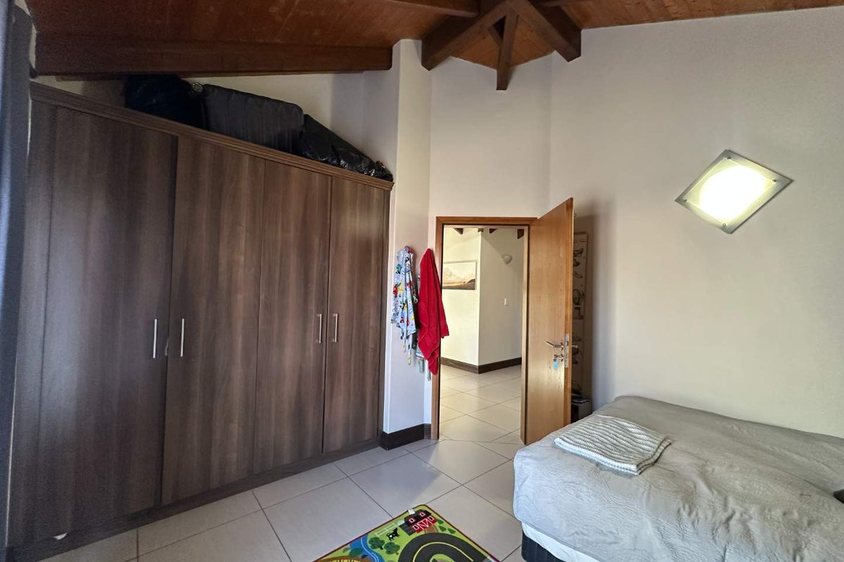A bedroom featuring high vaulted timber ceilings, tiled flooring, and a built-in wooden wardrobe.