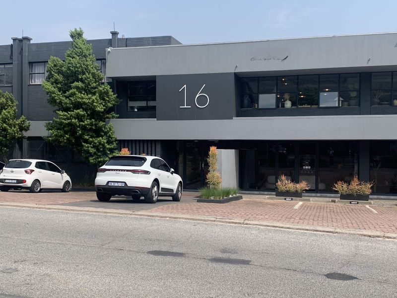 Modern office building exterior featuring a clean facade, large glass windows, and paved parking area.