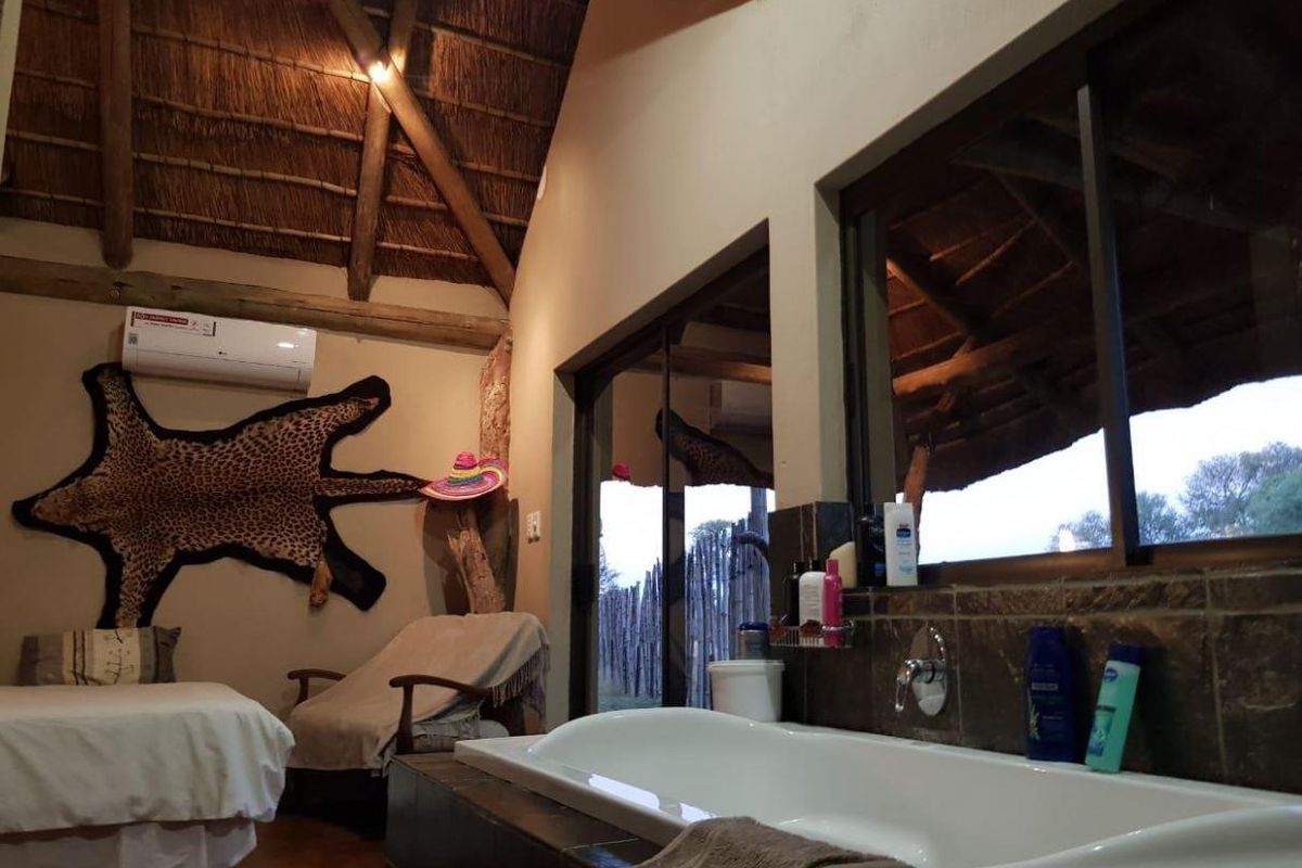 A unique bathroom featuring a high thatched ceiling with exposed timber rafters, a built-in bathtub, and sliding glass doors opening to the exterior.