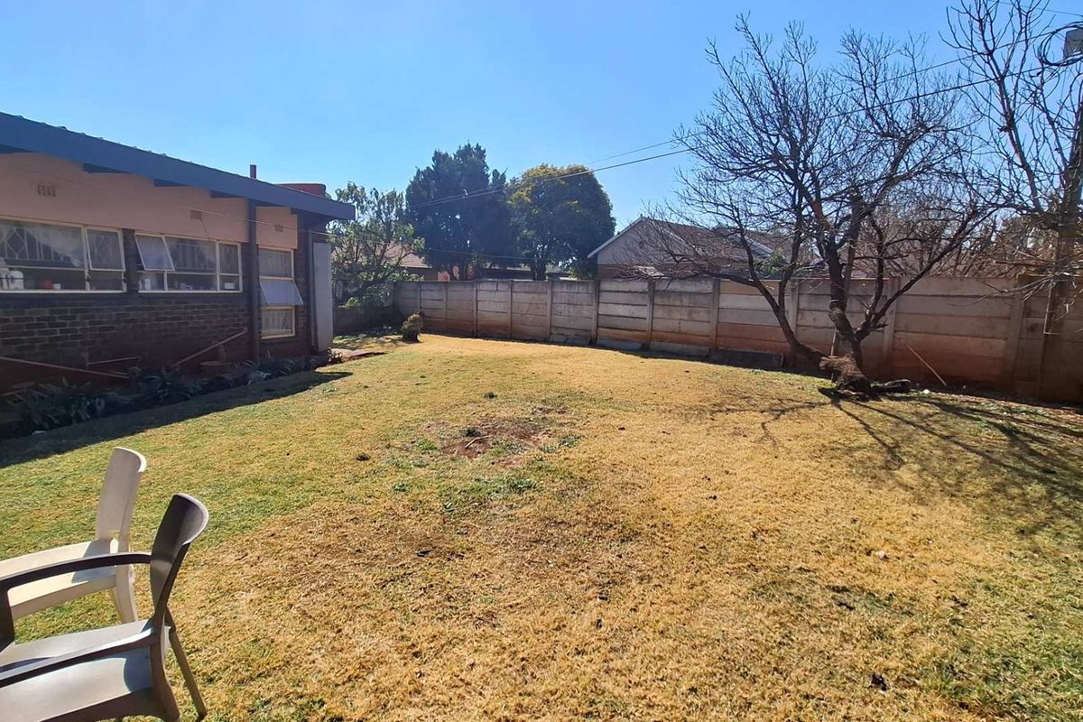 A spacious rear garden featuring a lawn area, enclosed by a precast concrete boundary wall, with a view of the brick house exterior.