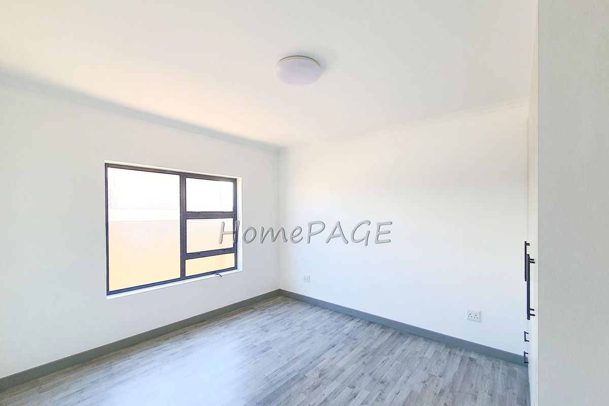 A bright, empty bedroom featuring modern grey wood-look flooring, white walls, and built-in cupboards.