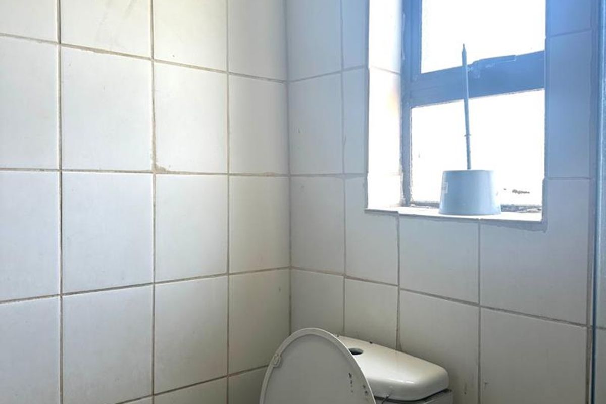 A compact bathroom featuring white wall tiles, a standard toilet, and a window providing natural light.