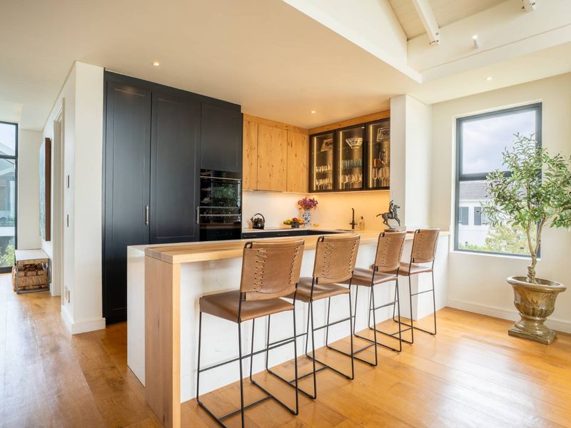 Modern kitchen featuring high-end cabinetry, stone breakfast bar, integrated appliances, and warm hardwood flooring in a bright, open-plan layout.
