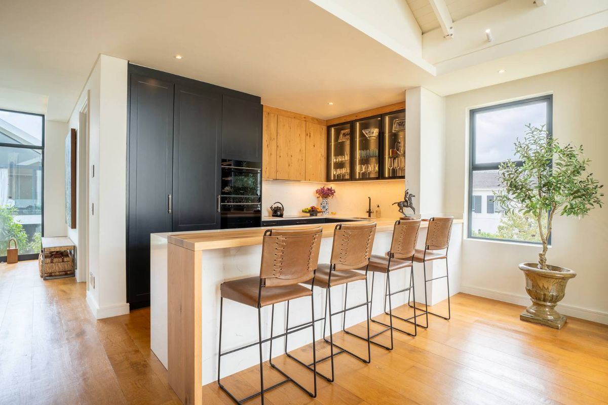 Modern kitchen featuring high-end cabinetry, stone breakfast bar, integrated appliances, and warm hardwood flooring in a bright, open-plan layout.