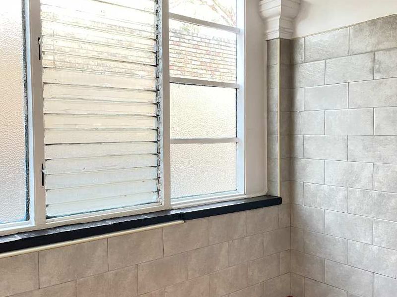 A functional kitchen area featuring louvered windows, tiled wall finishes, and red tiled flooring, offering a blank canvas for potential renovation.