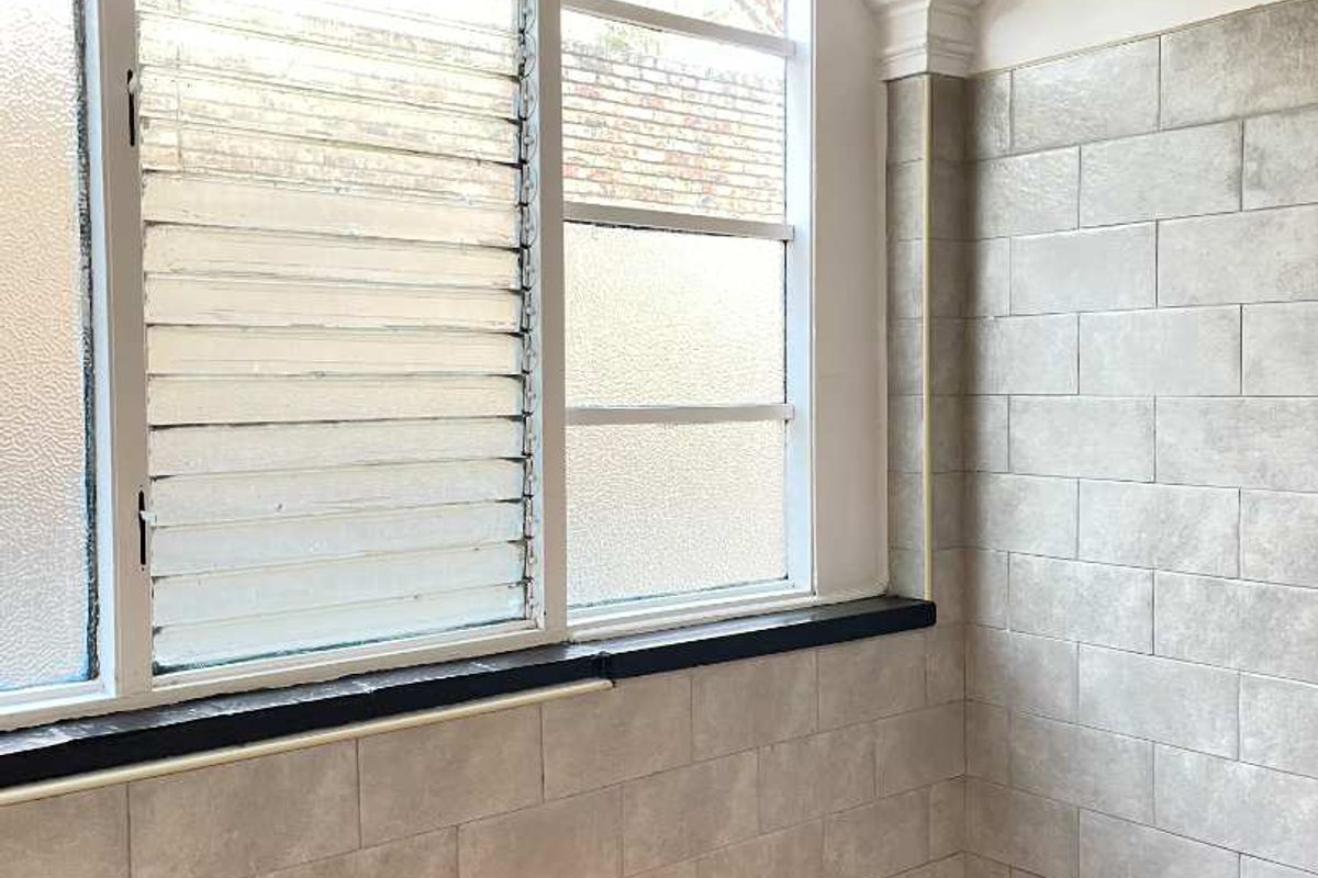 A functional kitchen area featuring louvered windows, tiled wall finishes, and red tiled flooring, offering a blank canvas for potential renovation.