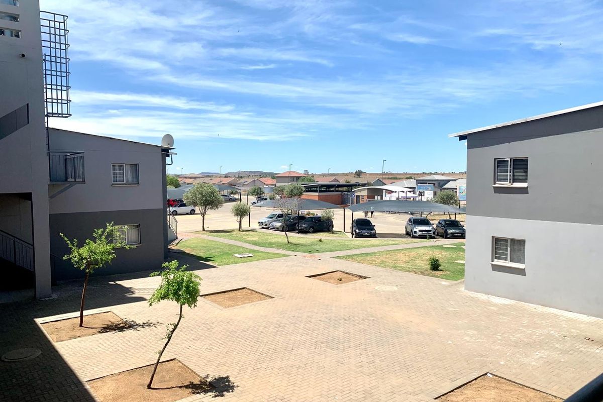 View of the apartment complex courtyard featuring paved walkways, landscaped garden beds, and covered parking areas.