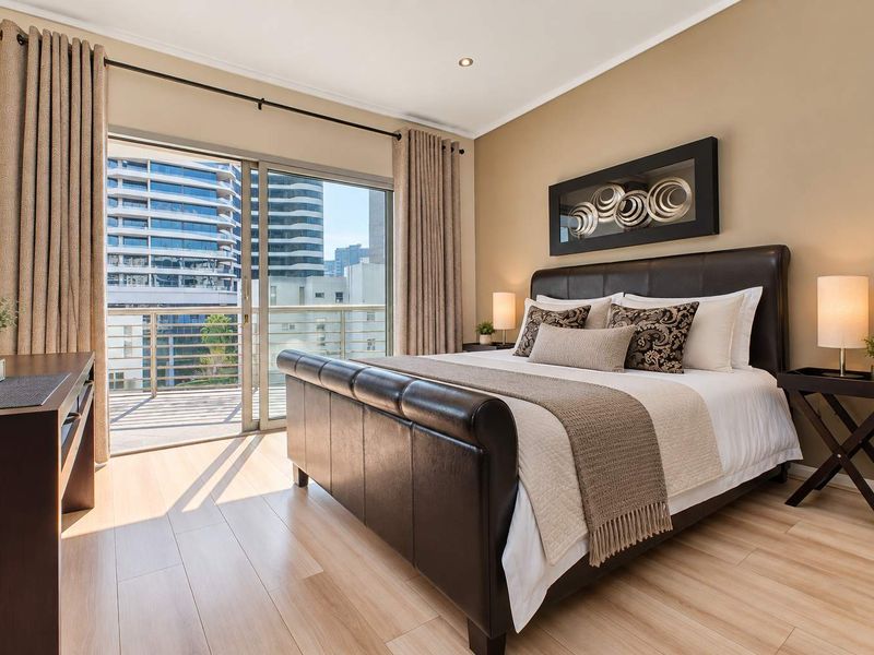 A well-maintained bedroom featuring laminate flooring, recessed lighting, and a sliding glass door providing direct access to a private balcony.