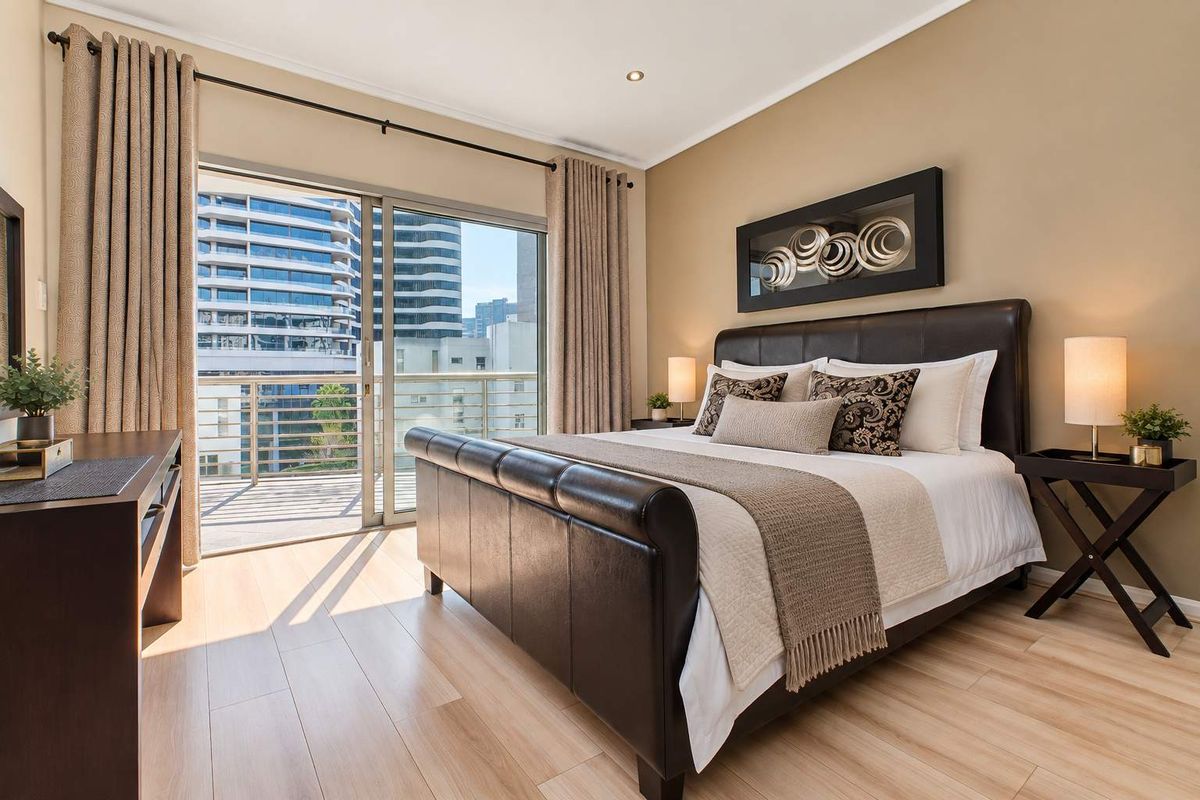 A well-maintained bedroom featuring laminate flooring, recessed lighting, and a sliding glass door providing direct access to a private balcony.