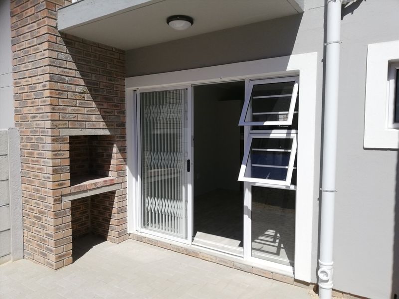 A covered patio area featuring a built-in brick braai, paved flooring, and a sliding glass door with security gate access to the interior.