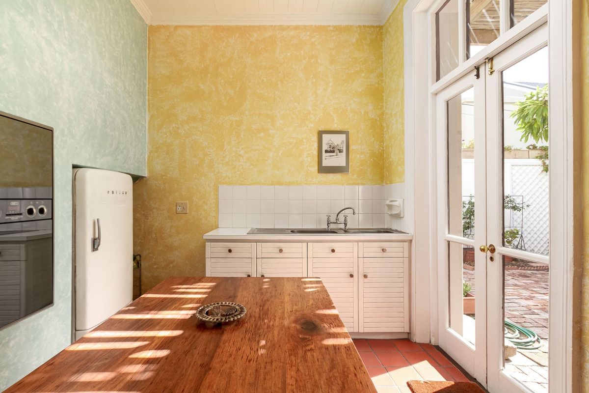 A bright kitchen featuring built-in cabinetry, a stainless steel sink, tiled backsplash, and direct access to an outdoor patio through glass french doors.