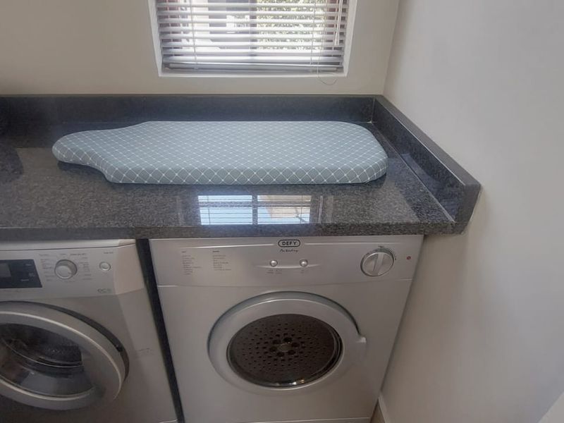 A functional laundry area featuring a dark granite countertop, built-in appliance housing, and venetian blinds for privacy.