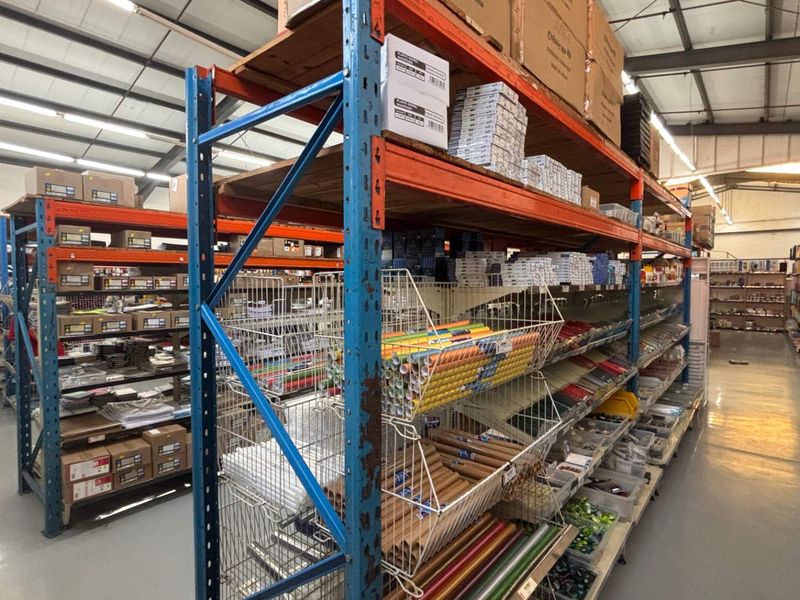 A spacious retail warehouse or storage area featuring industrial steel racking, exposed roof trusses, and durable epoxy-coated flooring.