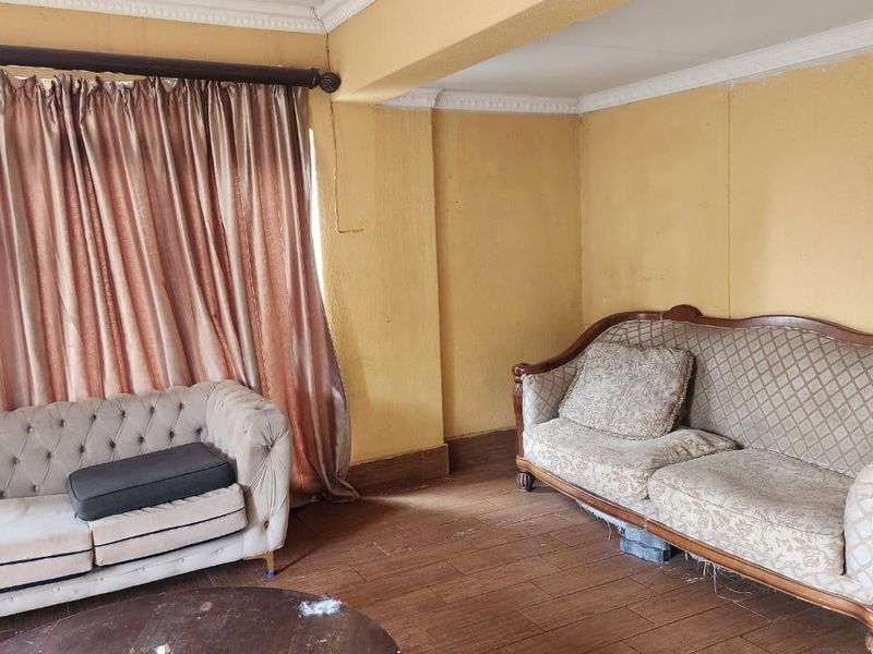 A living room featuring tiled flooring and crown molding, currently requiring cosmetic updates to the wall finishes to improve the overall aesthetic.
