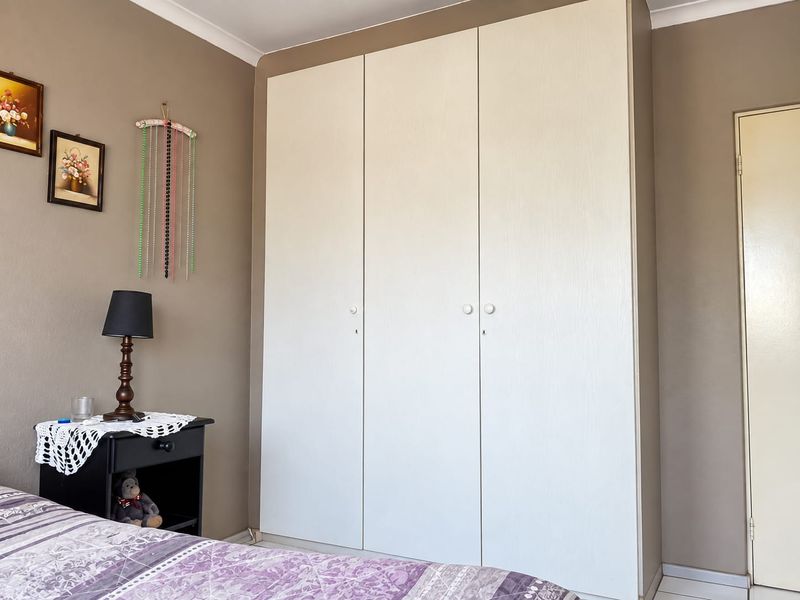 A bedroom featuring a large, white built-in wardrobe with three doors and neutral wall paint.