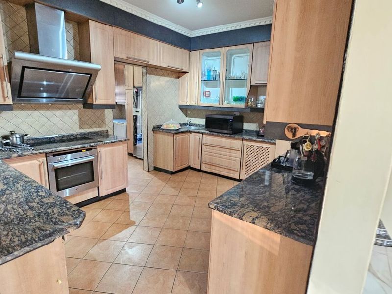 A functional kitchen featuring light wood cabinetry, granite countertops, built-in oven, extractor fan, and tiled flooring with an adjacent scullery area.