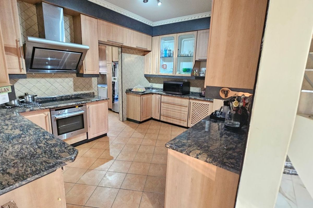 A functional kitchen featuring light wood cabinetry, granite countertops, built-in oven, extractor fan, and tiled flooring with an adjacent scullery area.