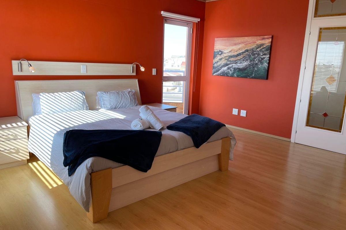 A bedroom featuring laminate flooring, a built-in headboard with integrated lighting, and a glass-paneled door leading to an outdoor balcony.