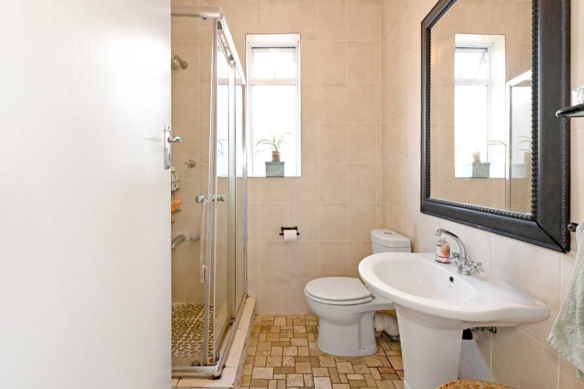 A functional bathroom featuring a glass-enclosed shower, pedestal sink, and neutral wall tiling.