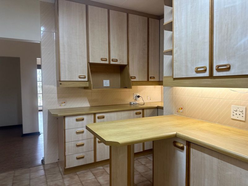 A functional kitchen featuring light wood-look laminate cabinetry, ample countertop space, tiled backsplash, and integrated under-cabinet lighting.