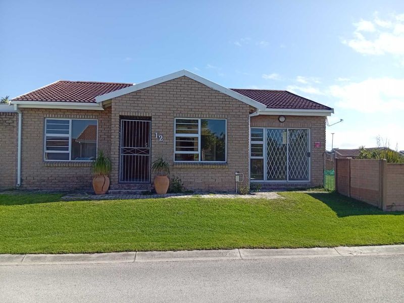 Front elevation of a face brick townhouse featuring a tiled roof, security gates, and a well-maintained front lawn.