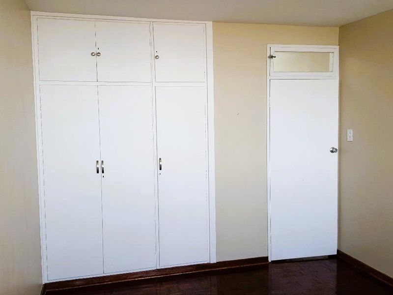 A vacant bedroom featuring built-in cupboards, wooden parquet flooring, and a standard internal door with a transom window.