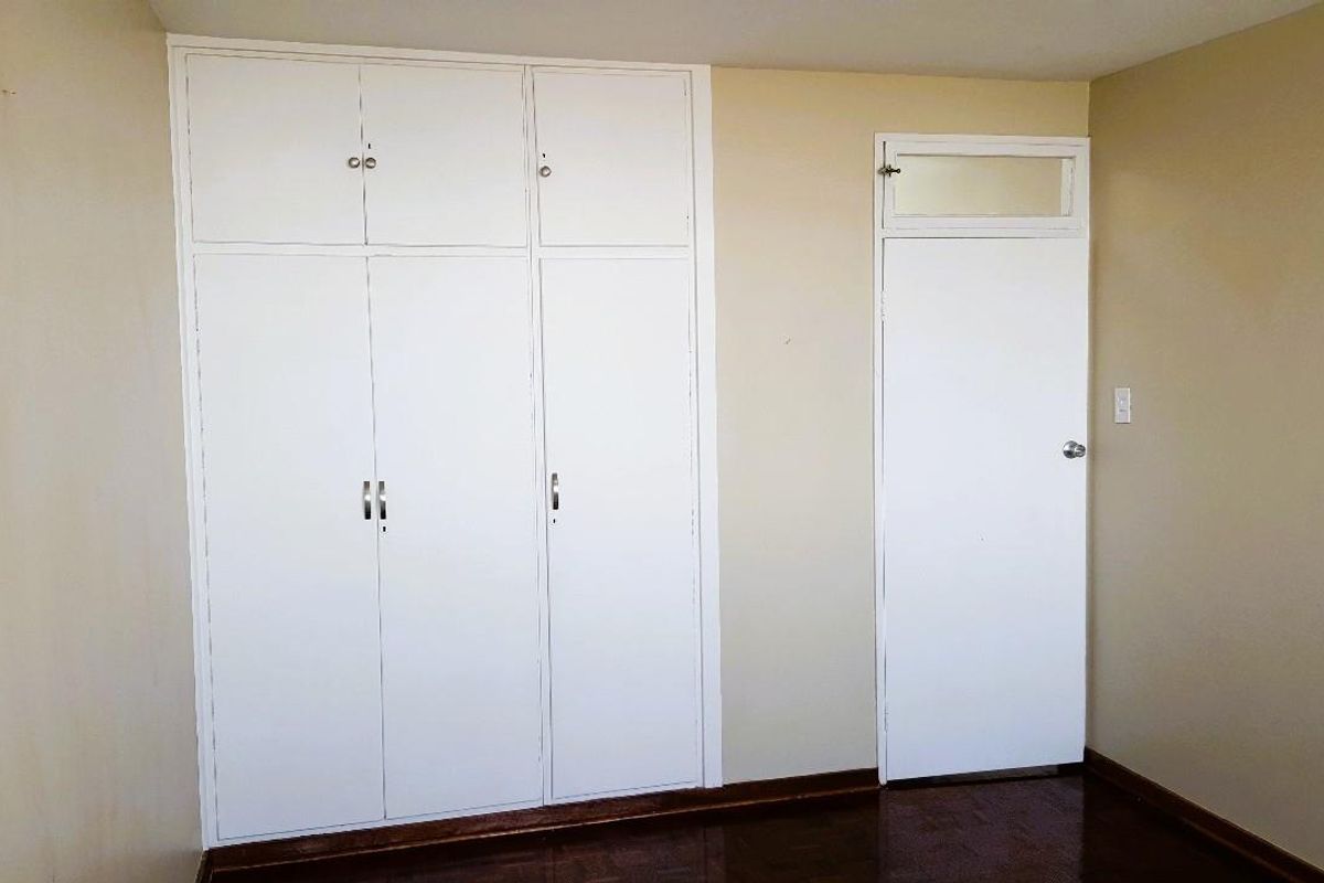 A vacant bedroom featuring built-in cupboards, wooden parquet flooring, and a standard internal door with a transom window.
