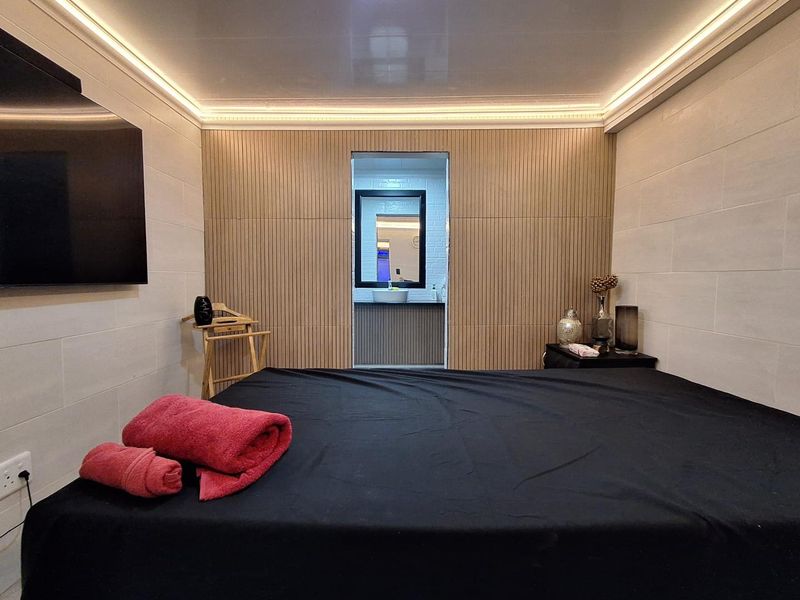 Modern bedroom featuring contemporary slatted wood wall paneling, recessed ceiling lighting, and direct access to an en-suite bathroom.