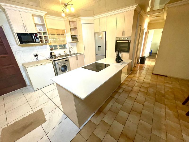 A functional kitchen featuring a central island with a hob, built-in oven, microwave, and ample cabinetry, finished with tiled flooring throughout.