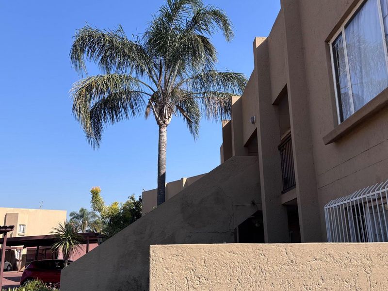 Exterior view of the apartment complex featuring stucco facade, security window bars, and an adjacent carport structure.