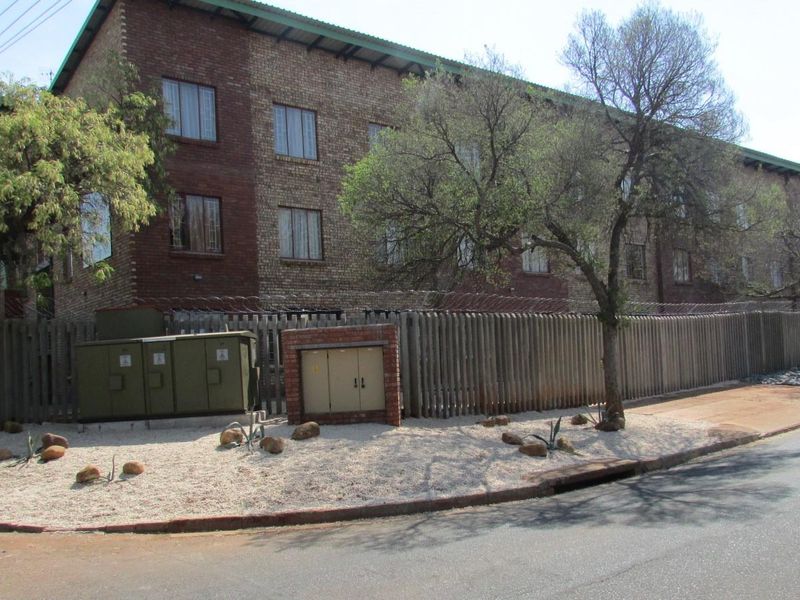 Exterior view of a multi-story brick apartment building featuring a perimeter fence with security razor wire and street-level utility infrastructure.