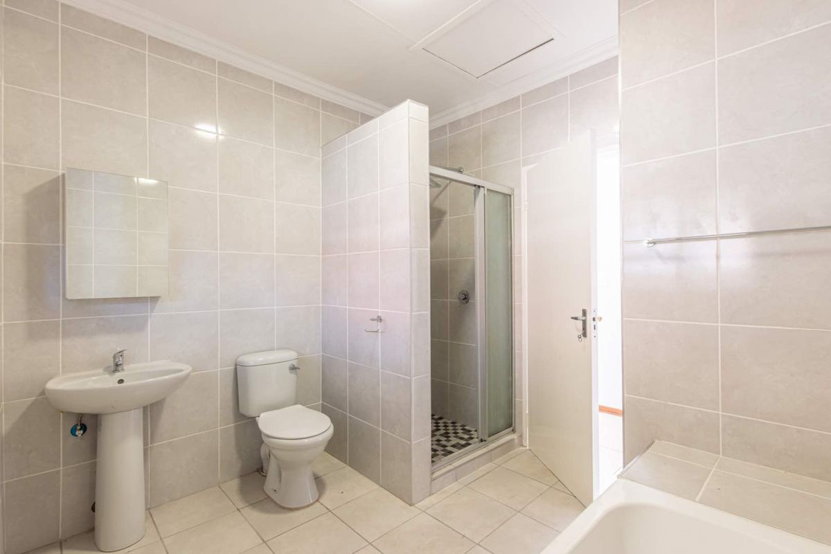 A functional bathroom featuring a pedestal basin, toilet, enclosed shower cubicle, and a bathtub with neutral wall and floor tiling.