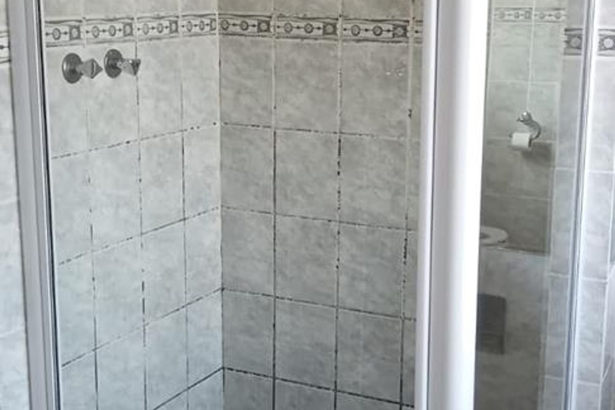A corner shower enclosure featuring tiled walls and flooring, requiring maintenance to the grout and tile surfaces.