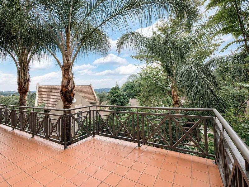 Spacious outdoor balcony featuring tiled flooring and a secure metal balustrade, offering elevated views of the surrounding landscape and mature trees.